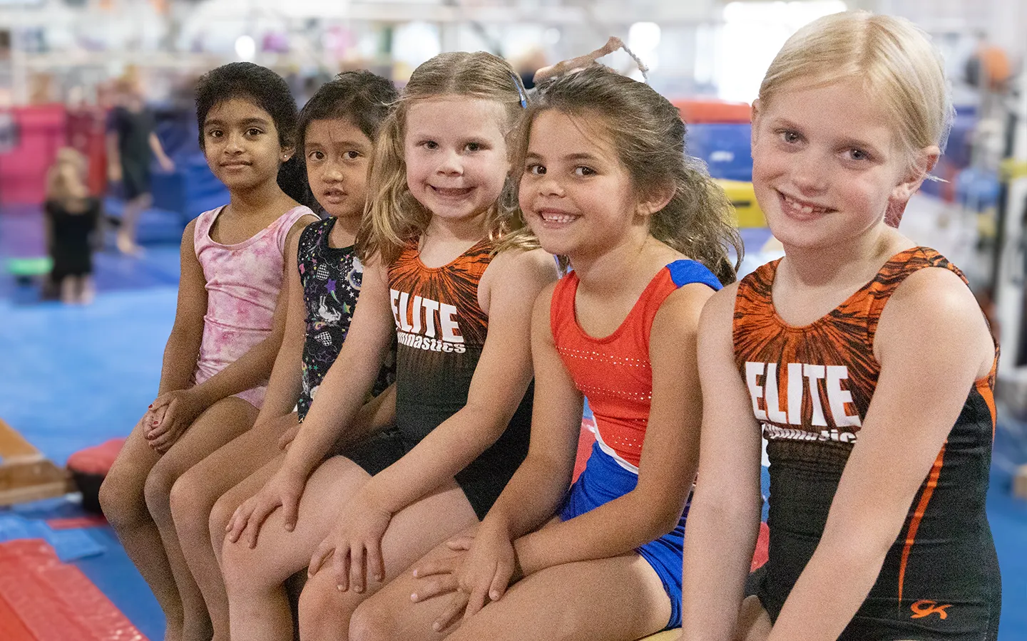 Five Tiger Girls gymnasts sitting together on a beam at EGA